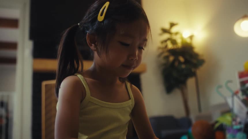 The video shows a quick sequence of two different young children first a toddler boy with short hair sits on the floor and looks at a small object in his hand he is wearing a blue tshirt the camera then cuts to a young girl with her hair in pigtails