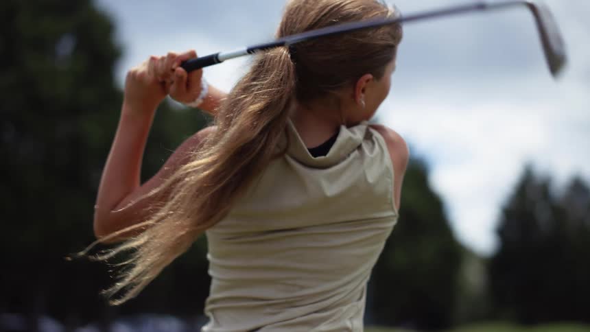 A young female golfer concentrates as she swings her golf club