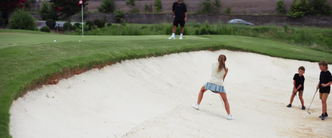 The girl hits the golf ball out of the sand trap