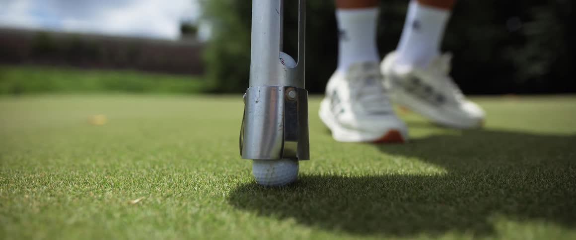 The person uses a device to pick up the golf ball