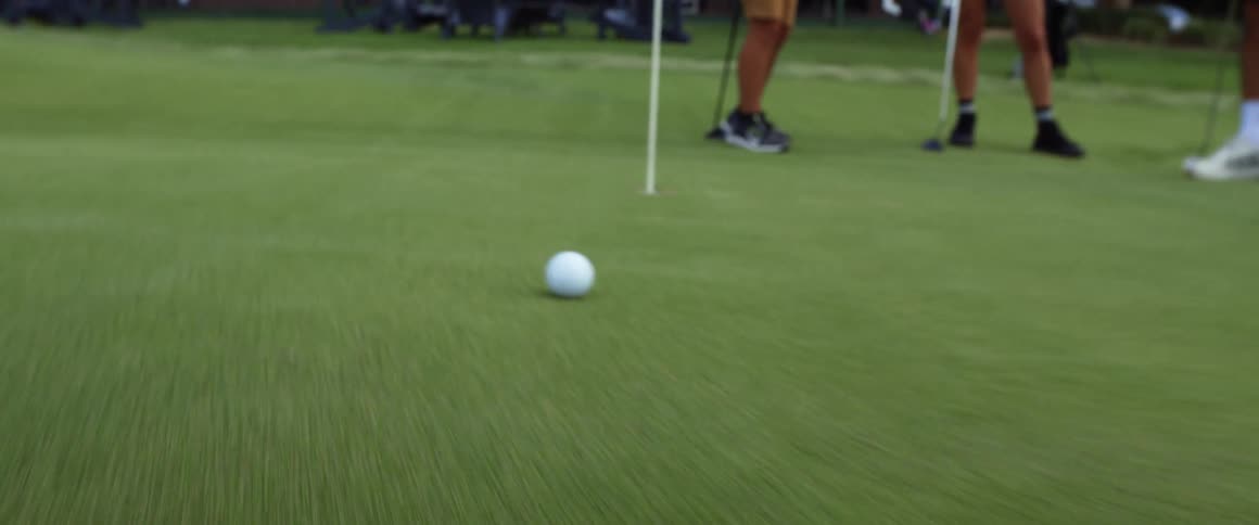 The video shows a golf club putting a golf ball on a green which rolls toward a hole with a flagstick the golf ball slows down as it approaches the hole but it ultimately stops right on the lip of the cup
