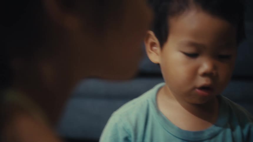 A toddler girl accompanied by a toddler boy to her side picks up a piece of a puzzle and holds against her face before throwing it back on the floor indoors