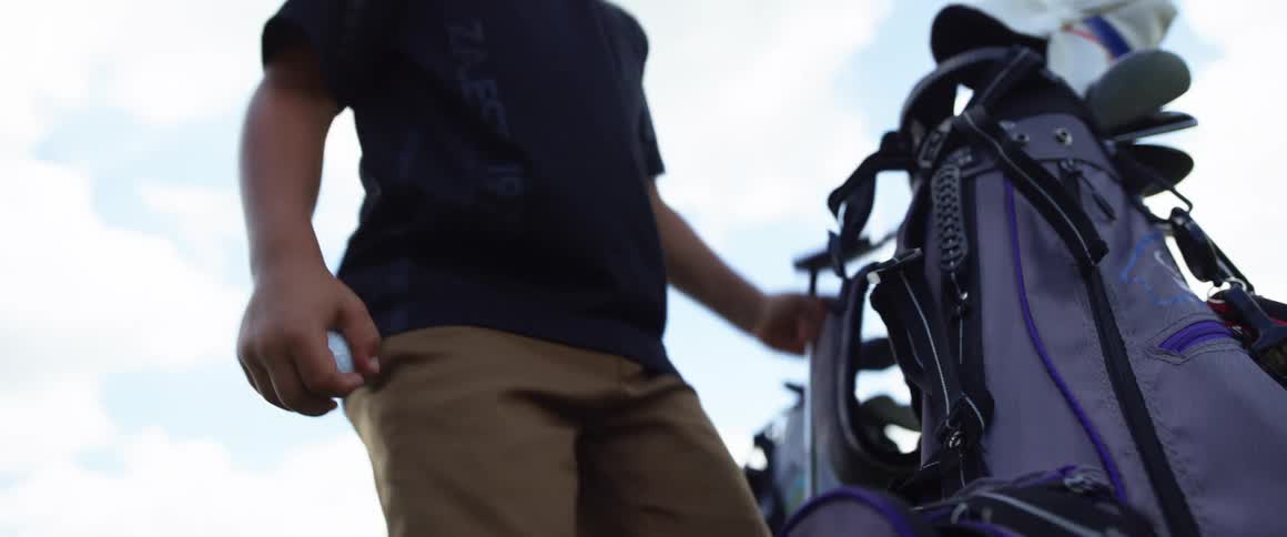Boy wearing a cap handling a golf bag