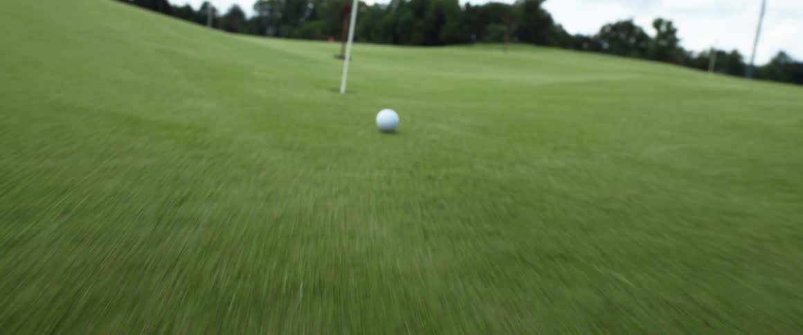 The video shows a golf putter hitting a golf ball which then rolls toward the hole the ball goes over the hole without dropping in