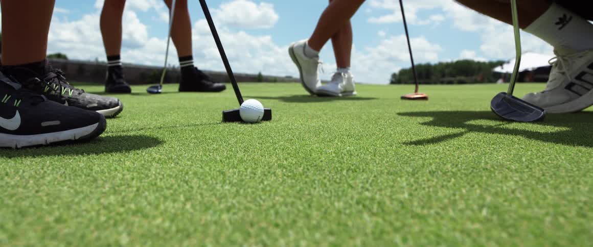 Golf ball positioned on the green surrounded by players with putters ready to strike
