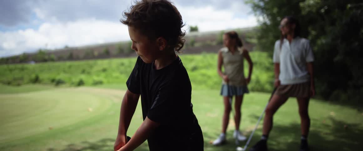 A boy playing golf with two young women outdoors during day time