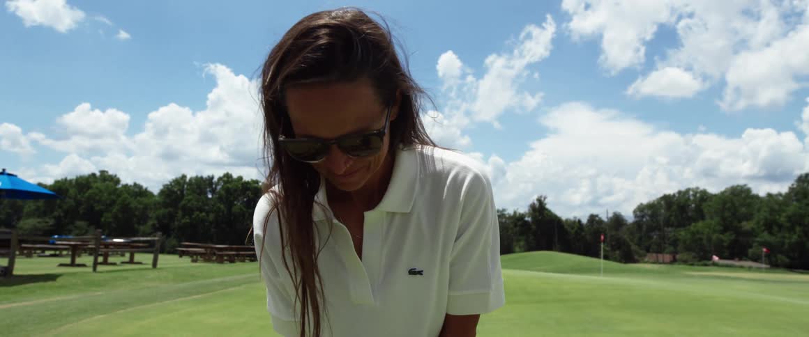 A woman wearing sunglasses takes a swing on a golf course