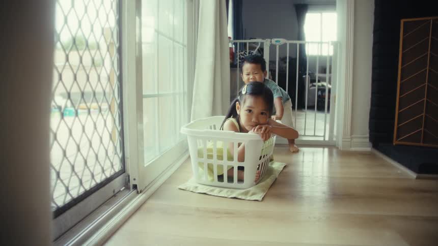 Two children play as one pushes the other in a laundry basket
