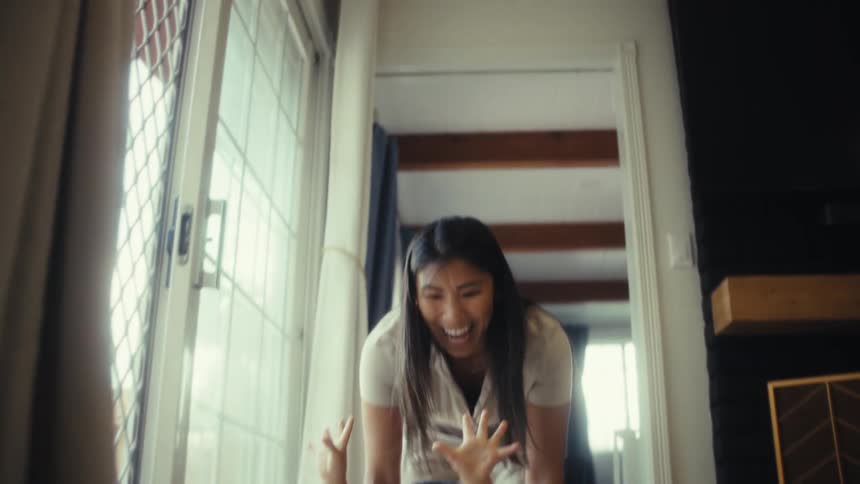 Male toddler smiling and lifting his arms in joy while a young woman playfully drags him around the floor on a plastic basket indoors during day time