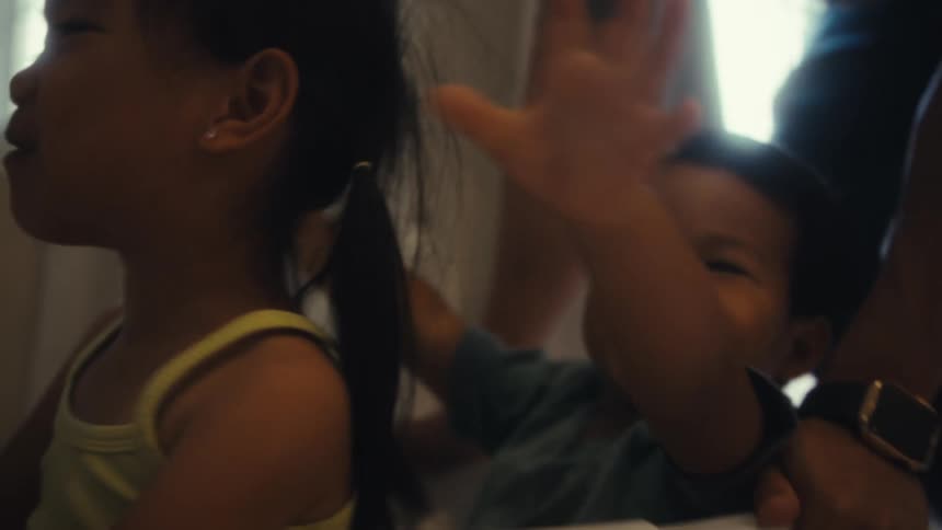 Adult person carrying two cheerful children in a laundry basket through the hallway of the house playing