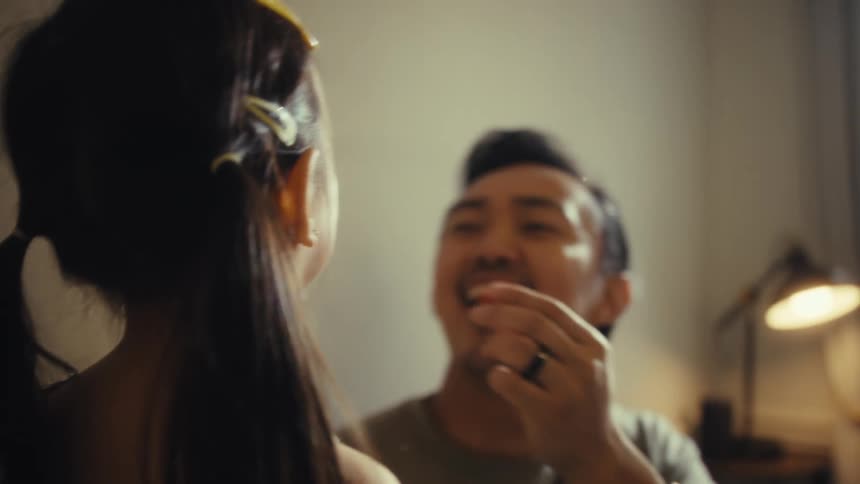 A closeup shot of a father and daughter shows the girls back to the camera the man is looking at his daughter and smiling as he puts a berry in his mouth