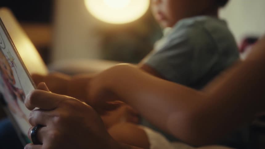 Two children reading and pointing to a book in an indoor setting while an adult holds the book