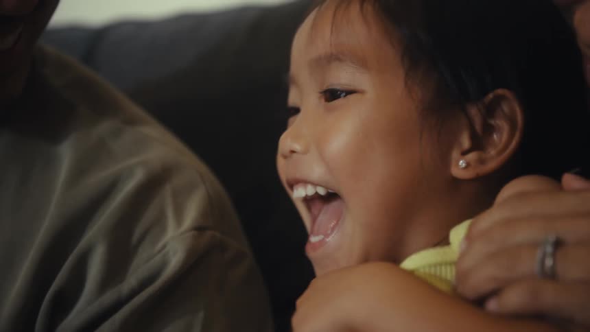 A girl laughs in her parents arms