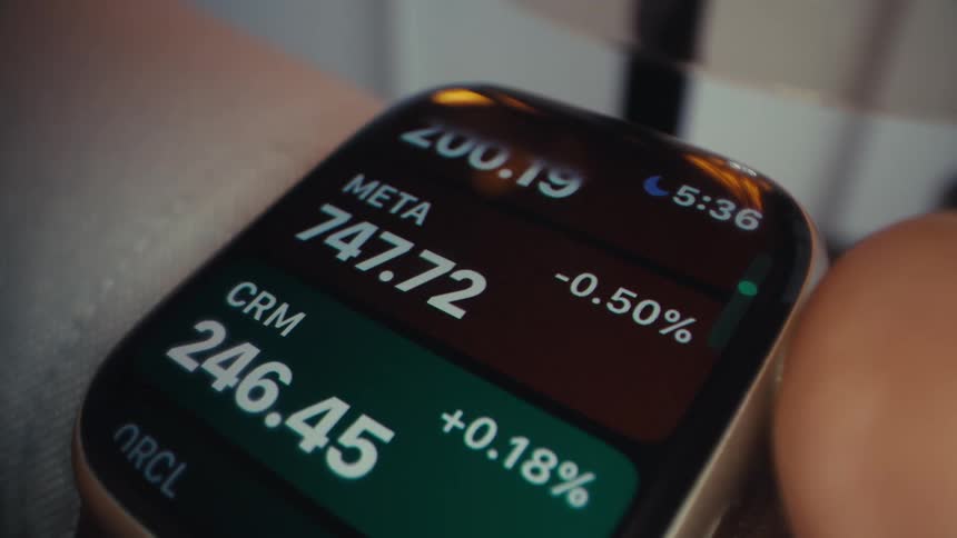 The video shows a closeup shot of a wrist with a watch displaying financial information including stock prices and cryptocurrency values the numbers for various tickers like goog msft and btc can be seen changing