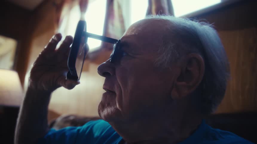 Elderly man using binoculars in front of a smartphone