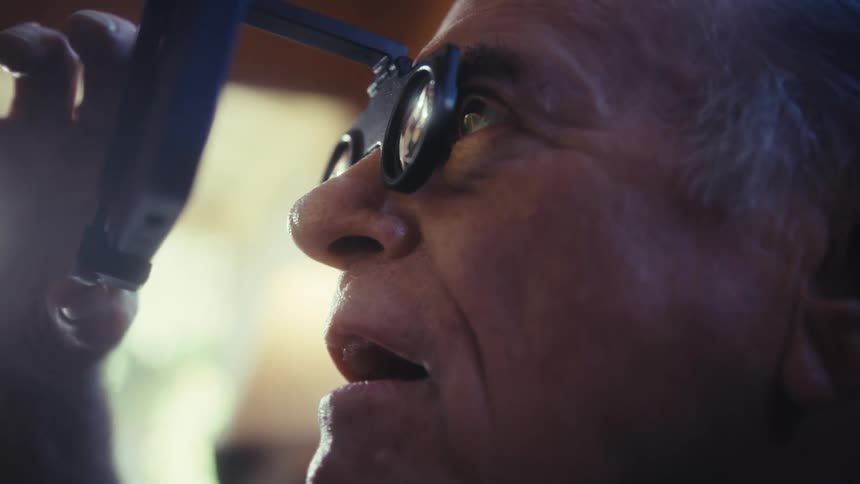 A smiling person with white hair holds a magnifying device attached to a smartphone to their face as they look upwards
