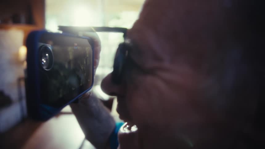 Elderly man with magnifying glasses using a smartphone