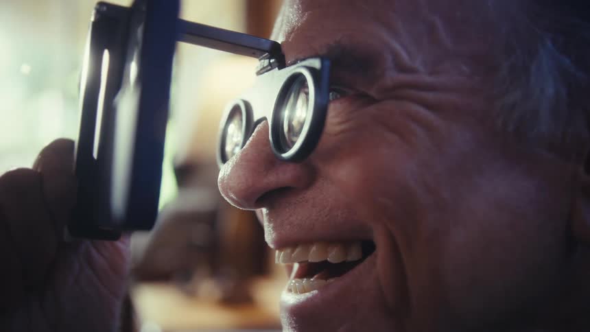 Smiling man looks closely through a lens viewer