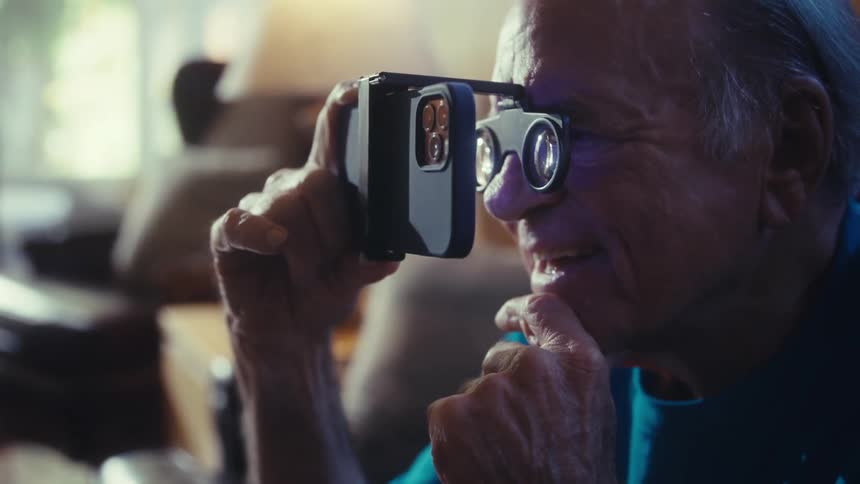 Elderly man wearing vr glasses to watch content on his phone up cloe as he smiles while watching midday in his living room