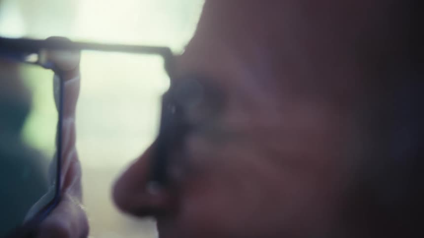 A person looks through a magnifying lens at a screen on a device while their face and hand are visible