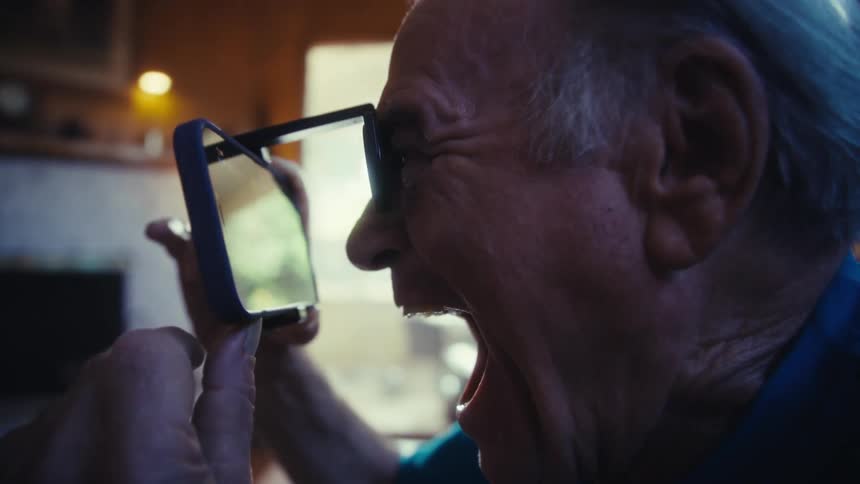 A persons face in profile holds a smartphone and looks through a lens with an expression