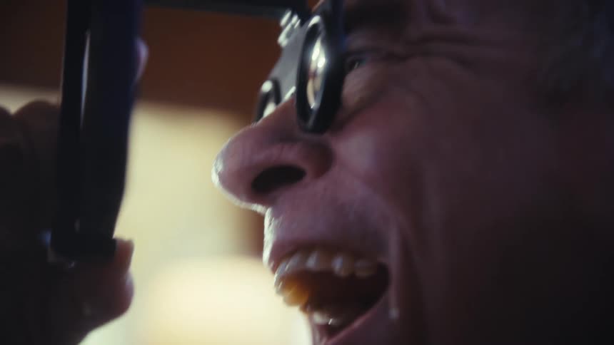 Elderly man smiling while holding a cellphone close to his face