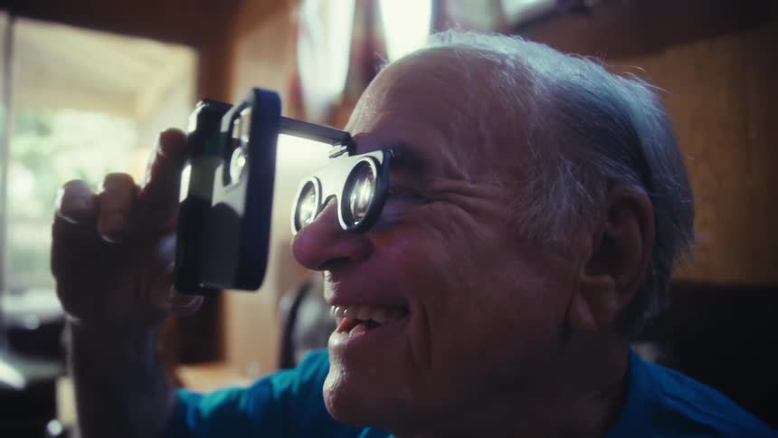 Elderly man looking closely through a magnifying glass of glasses and interacting with a smartphone