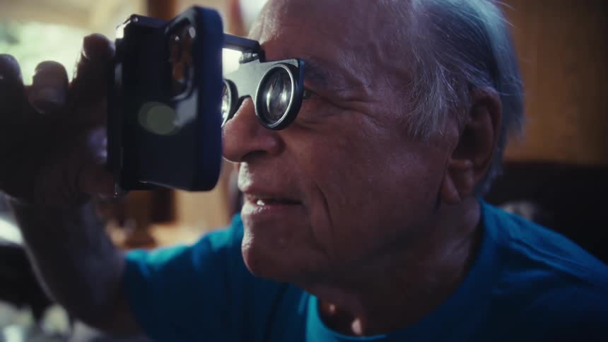 The man is using magnifying glasses to look at his cell phone