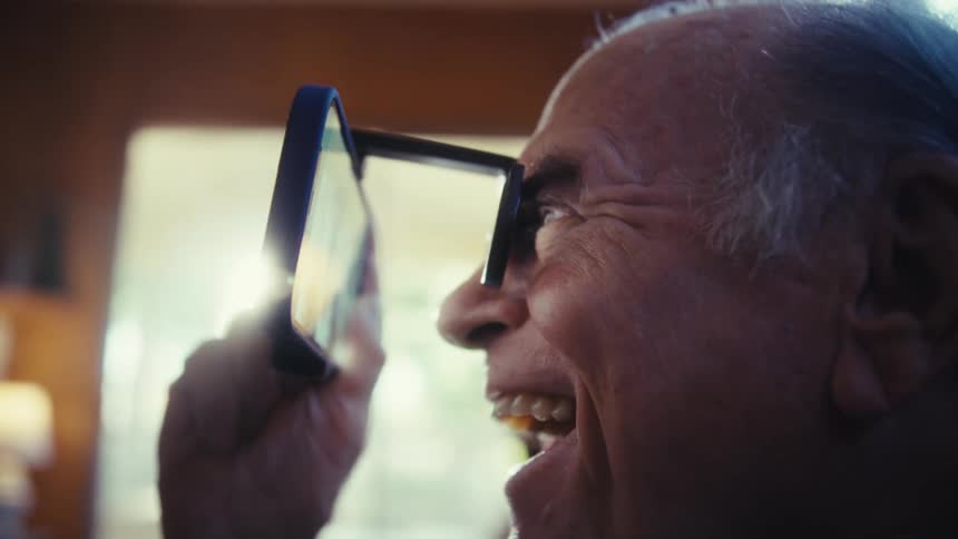 The video shows a man with white hair wearing what looks like a pair of binocularstyle glasses with a phone attached he looks down at the phone with an expression of awe and surprise then breaks into a wide smile as he moves his gaze upward