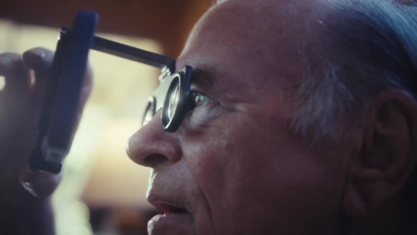 Elderly man closely observing through a magnifier with glasses