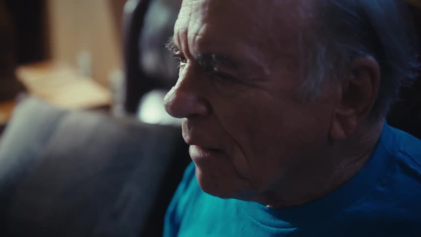 An elderly man in a football shirt yells at the television