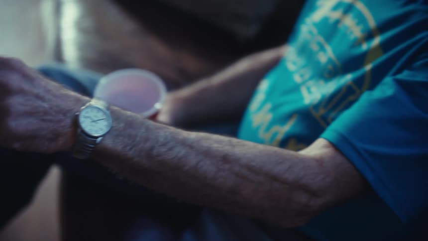 A person sits on a couch holds a remote control in a hand and looks towards a television