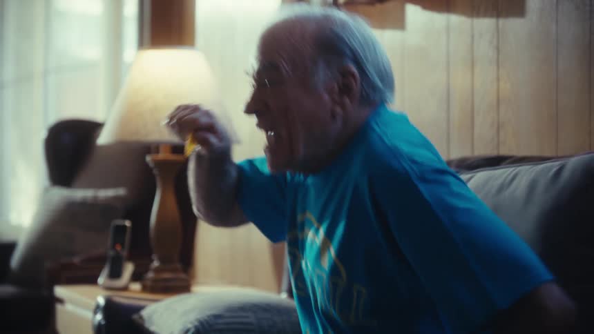 Elderly man sitting on sofa in living room celebrating happily in vibrant manner