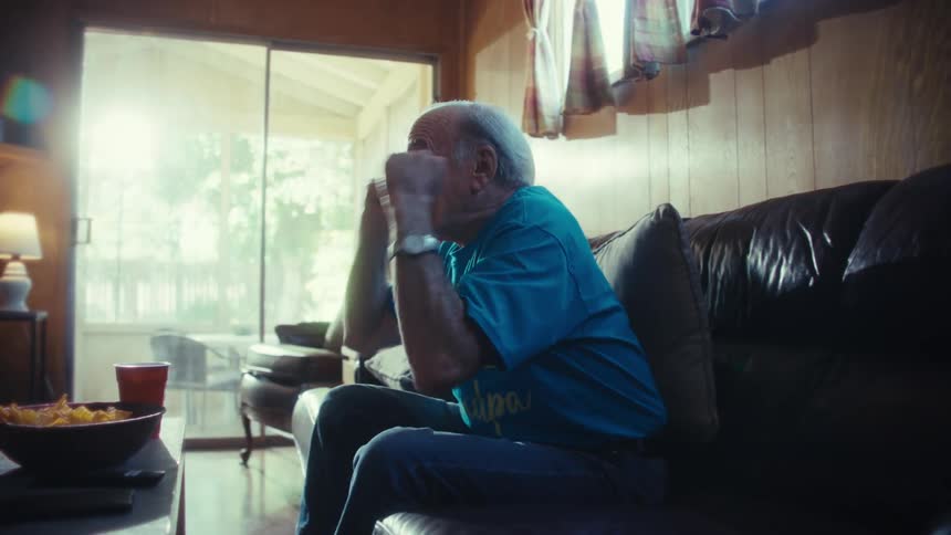 A person on a couch gestures with their arms while watching a television in a room with a fireplace and windows