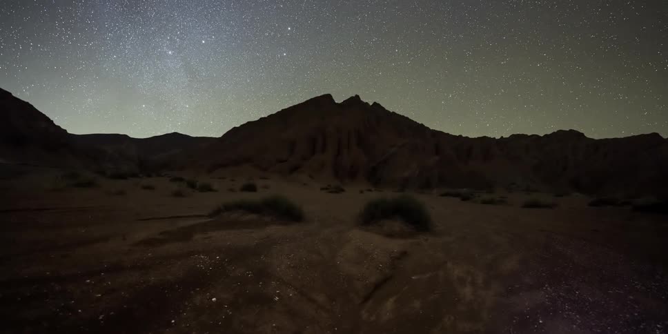 A mountain in the wilderness surrounded by barren land as day transitions to night