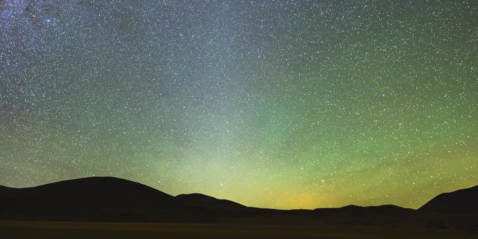 Darkeness falls as the stars of the milky way galaxy glow as they move over mountains in the night sky