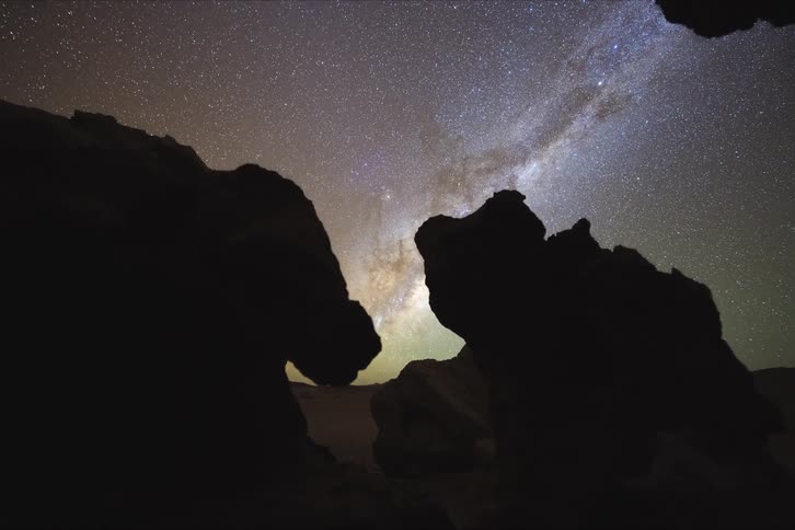 Upward view of ruins and mountains in silhouettes and the starry sky at night