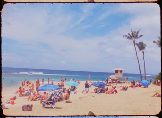 A shoreline with people and umbrellas separates a body of water with waves and a sky with clouds