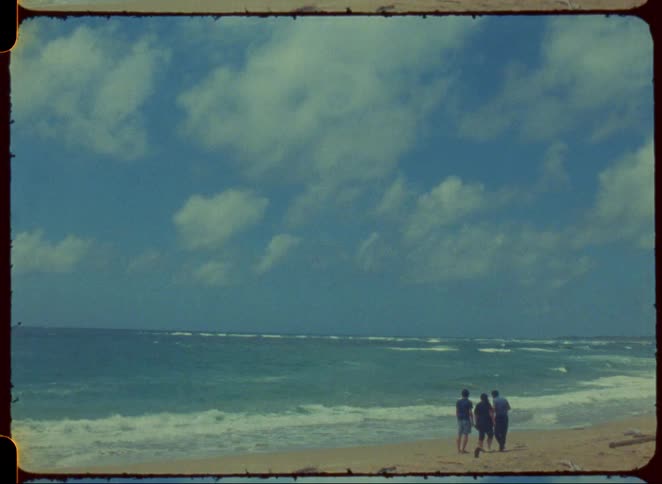 Three people on sandy shoreline watching waves roll in at the beach