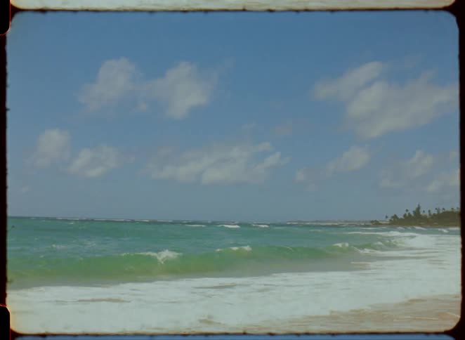 The video shows a beach scene with turquoise waves rolling onto a shore lined with palm trees the sky is blue with scattered white clouds and a watermark from filmsupply is visible in the center of the frame