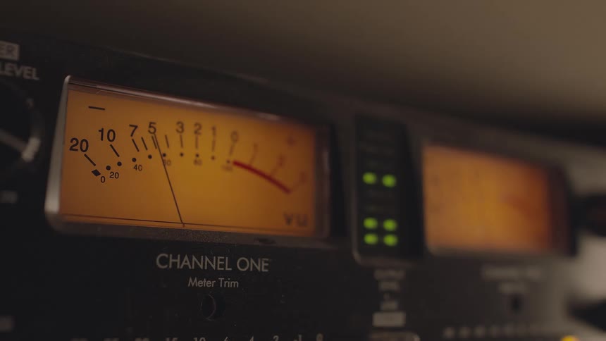 A large orange and black audio meter with a needle that moves up and down is next to a line of green indicator lights that flash on and off