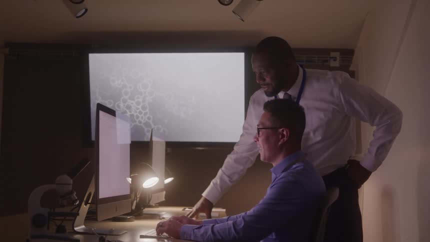 A man leans over the desk pointing at the monitor