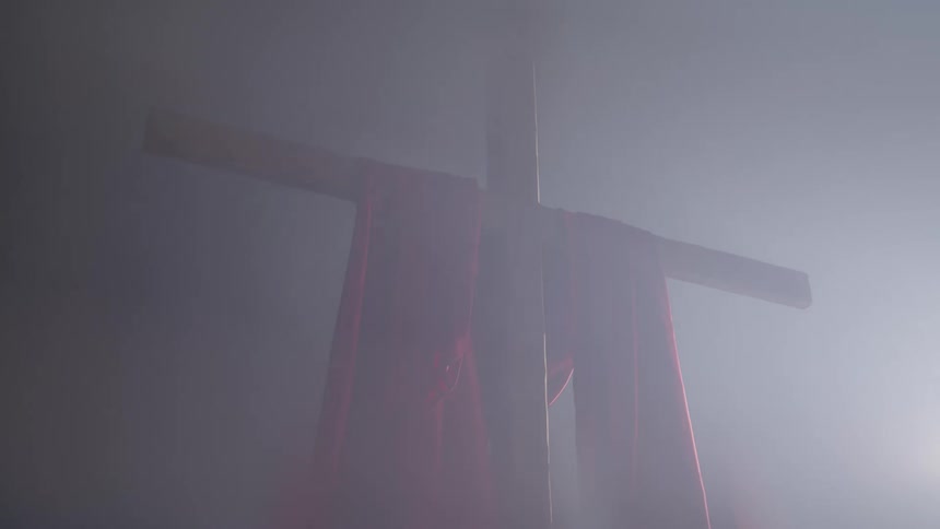 Wooden cross with a red cloth draped over it in a misty setting