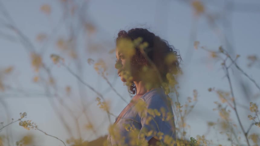 Curlyhaired woman among yellow flowers at sunset