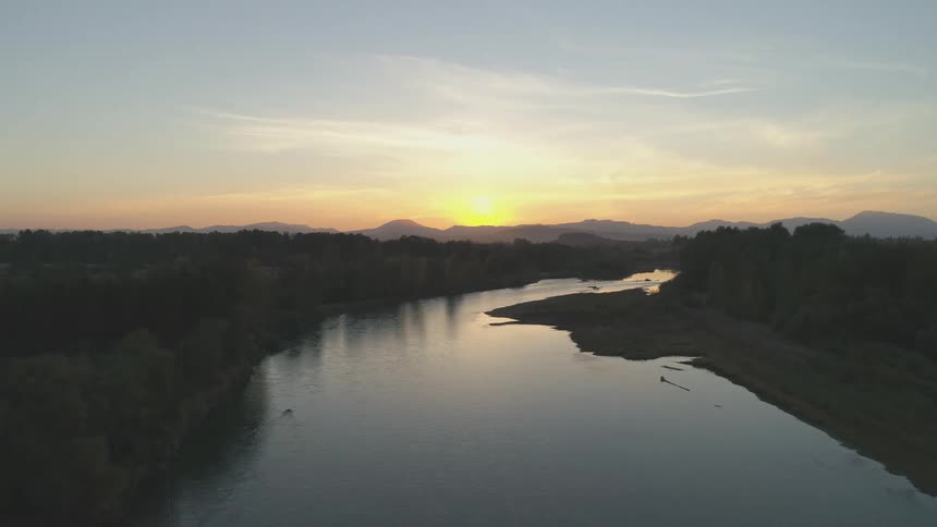 River surrounded by a forest with a mountain range in the background during dusk or dawn