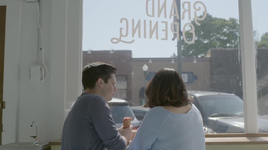 A man and woman eat near a window