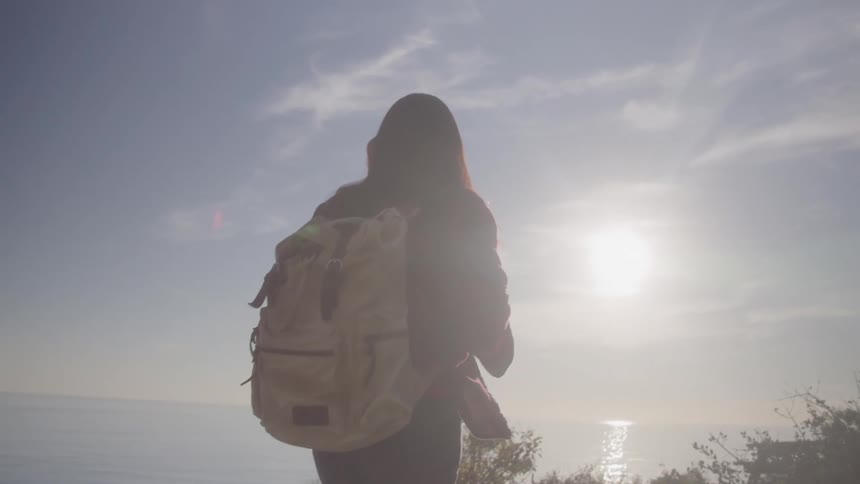 Woman with backpack hiking with the sun on the horizon