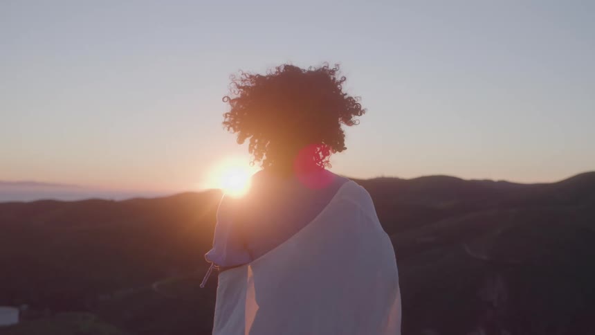 The woman is standing on a mountain as the sun rises