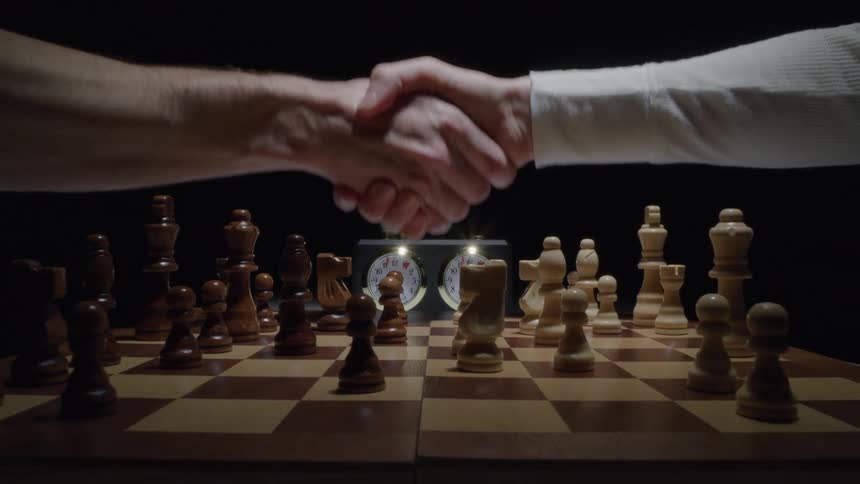 Two hands shaking hands in a game of chess