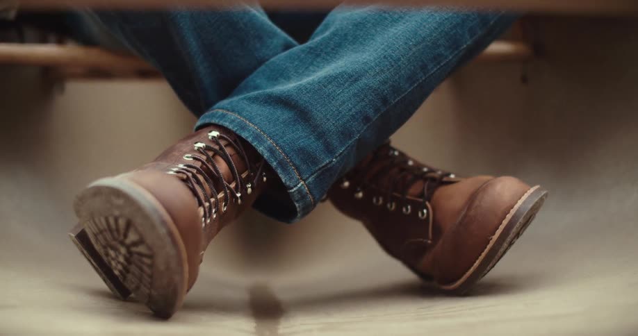 A person wearing boots and jeans sitting on a wooden platform outdoors